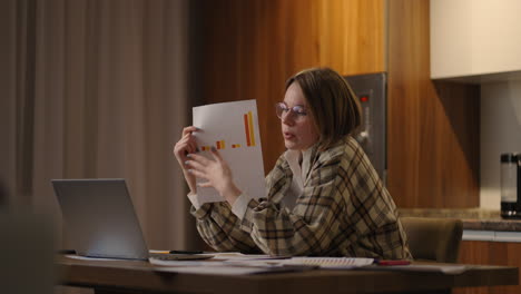 A-young-woman-with-glasses-at-home-shows-a-graph-Video-call-and-conference-with-demonstration-and-analysis-of-documents-and-schedules.